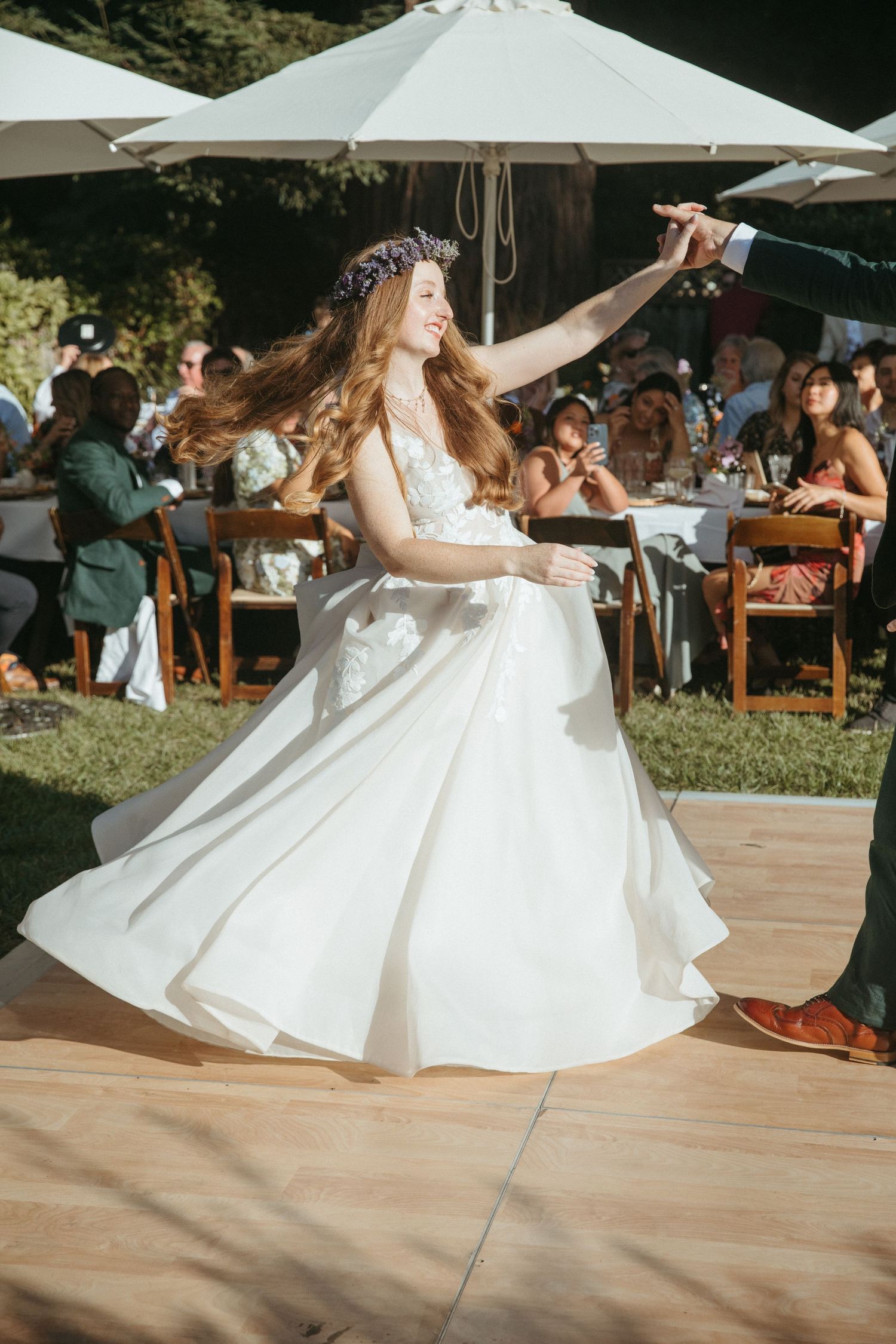 Bride in flowing white dress twirls during outdoor wedding reception dance under white umbrellas.