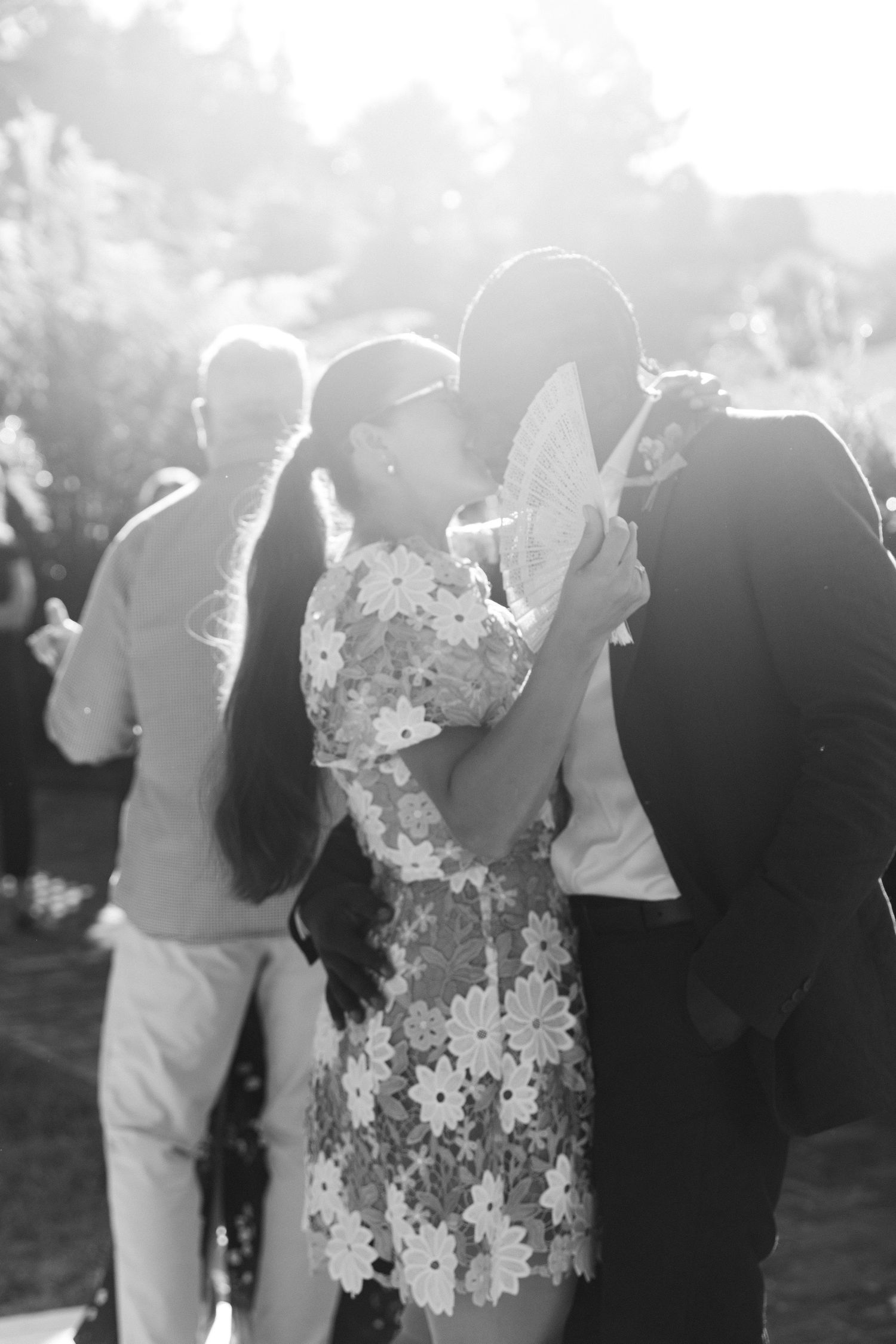Black and white wedding photo showing couples dancing together at an outdoor reception in soft sunlight.