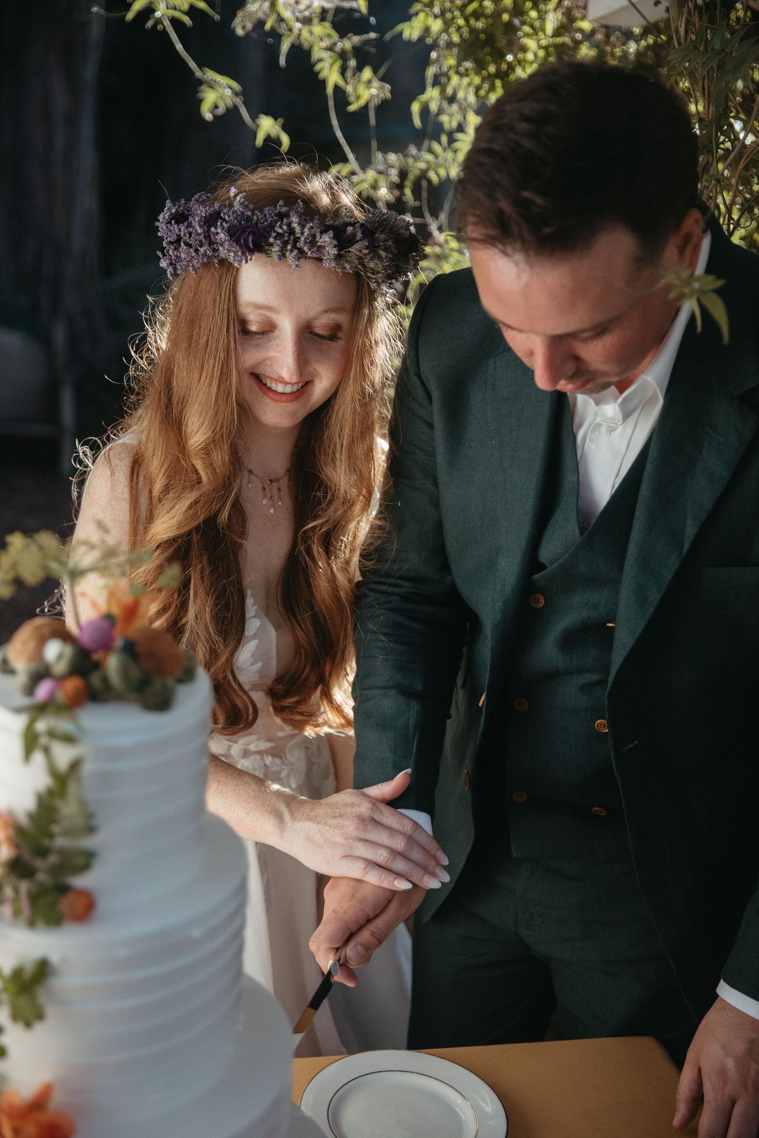 Couple in wedding attire sharing a moment while cutting their floral-decorated wedding cake.