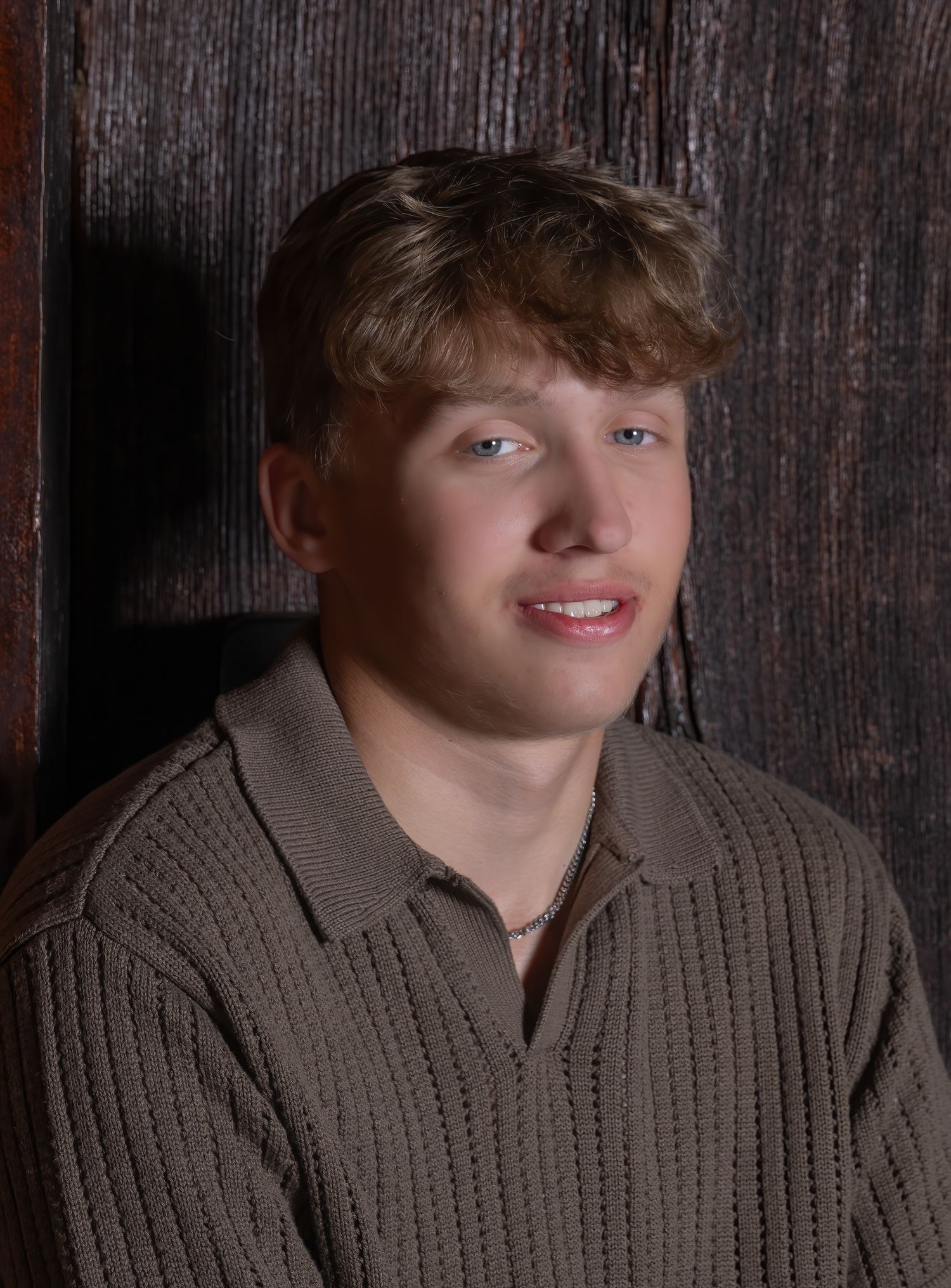Portrait of person in brown knit sweater against dark wooden background.