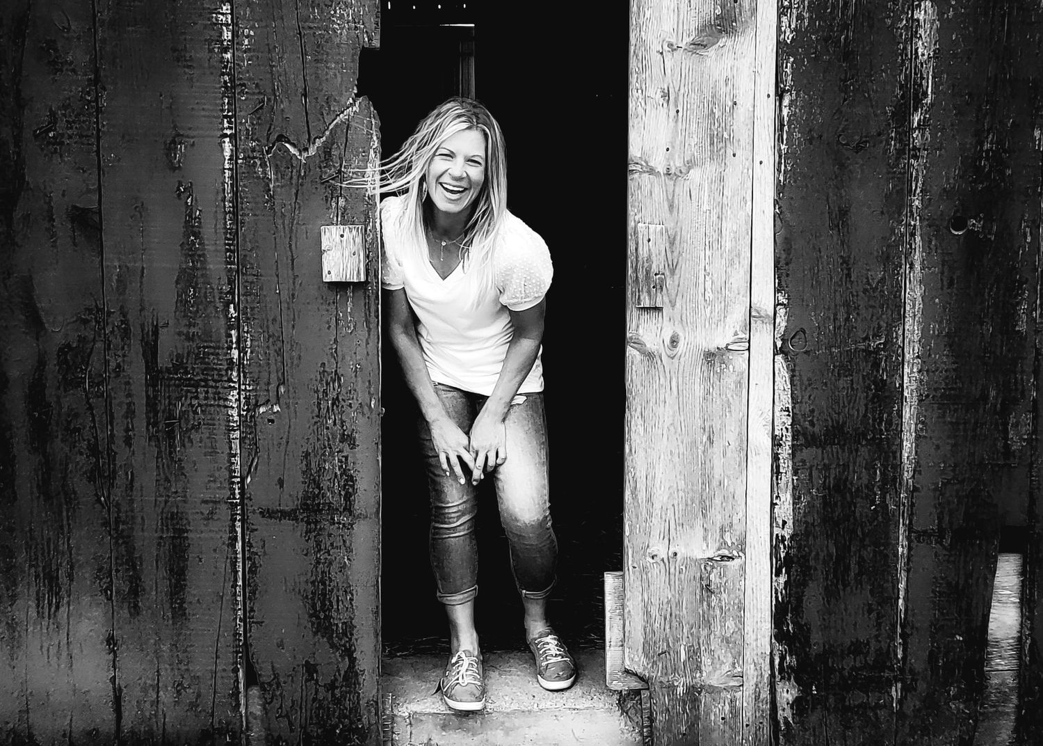 New property owner standing inside her barn door, laughing joyfully. She is surrounded by the sun washed barn boards.