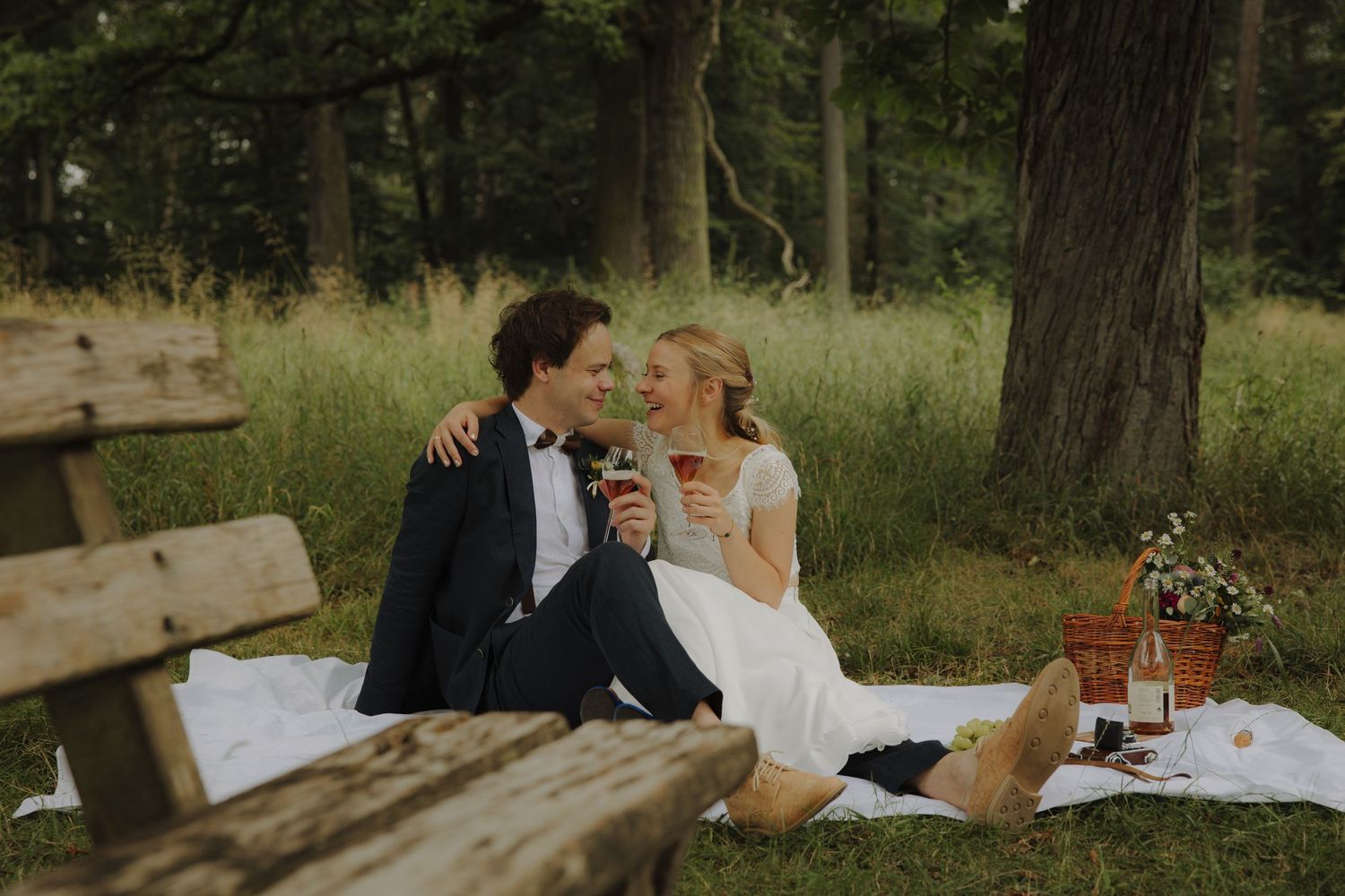 Newlyweds having a romantic picnic on a blanket in a woodland setting.