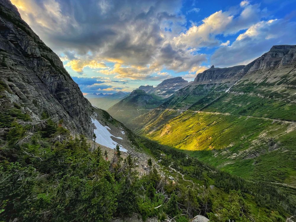 The sun creeps around a large mountain coloring the landscape in a bright yellow at Glacier National Park