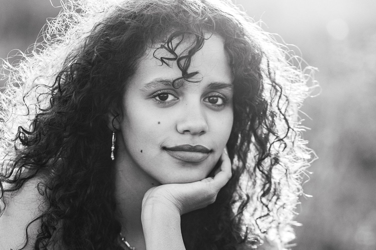 A woman with naturally curly dark hair poses in front of a blurred background in a black and white portrait for her senior photoshoot