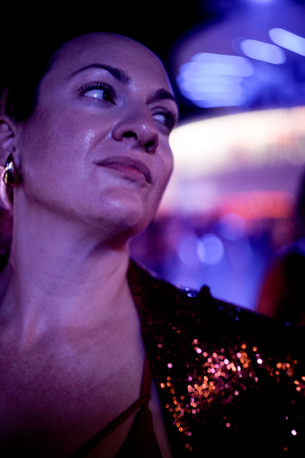 Close-up portrait with sparkly attire under blue and purple lighting.