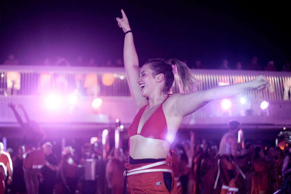 Energetic dancer with raised arms performs under purple stage lights.