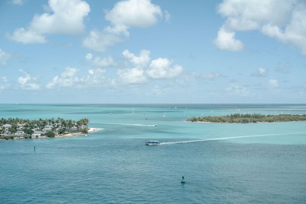 Aerial view of turquoise waters surrounding tropical islands with palm trees and boats in the distance.
