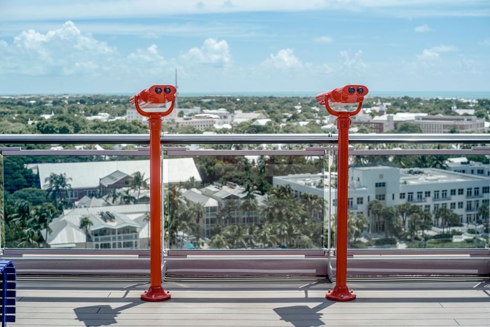 Two orange viewing scopes mounted on a deck railing with cityscape and ocean views.