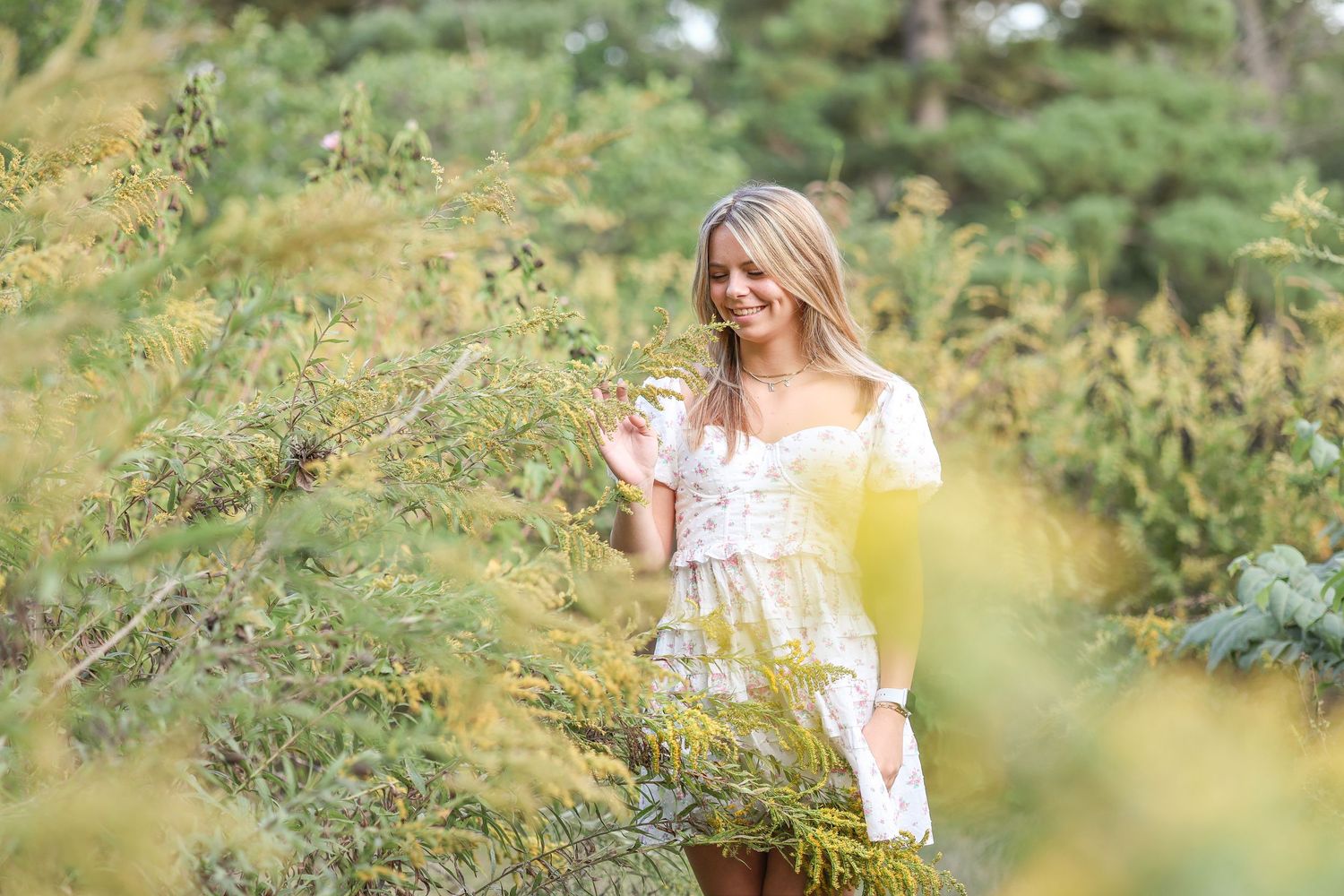 A woman in a white summer dress stands among wildflowers in a sunny garden setting.