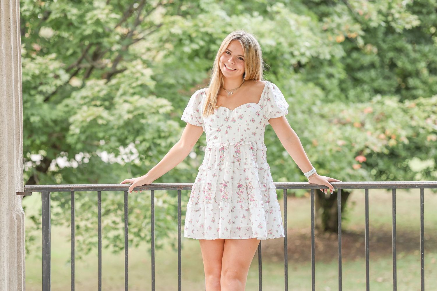A floral dress outfit paired with white boots creates a romantic look by a garden railing.