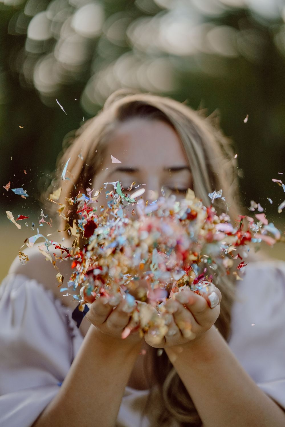 Hands blow colorful confetti creating a magical graduation photo with bokeh background.