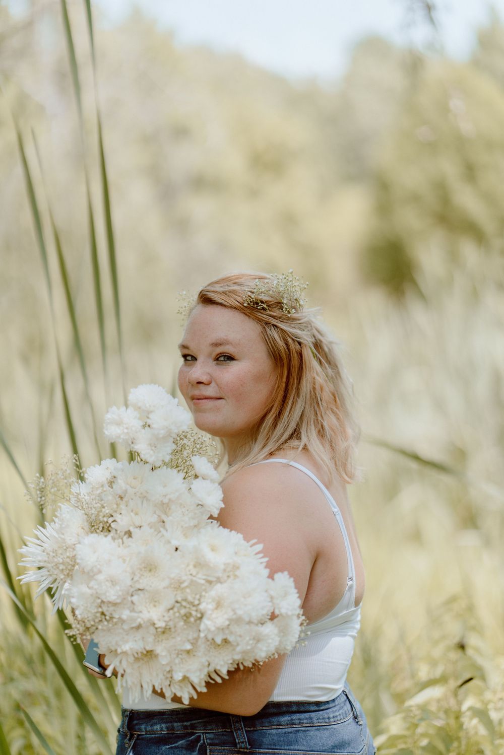 An ethereal outdoor portrait with white flowers and soft natural lighting in a meadow setting.