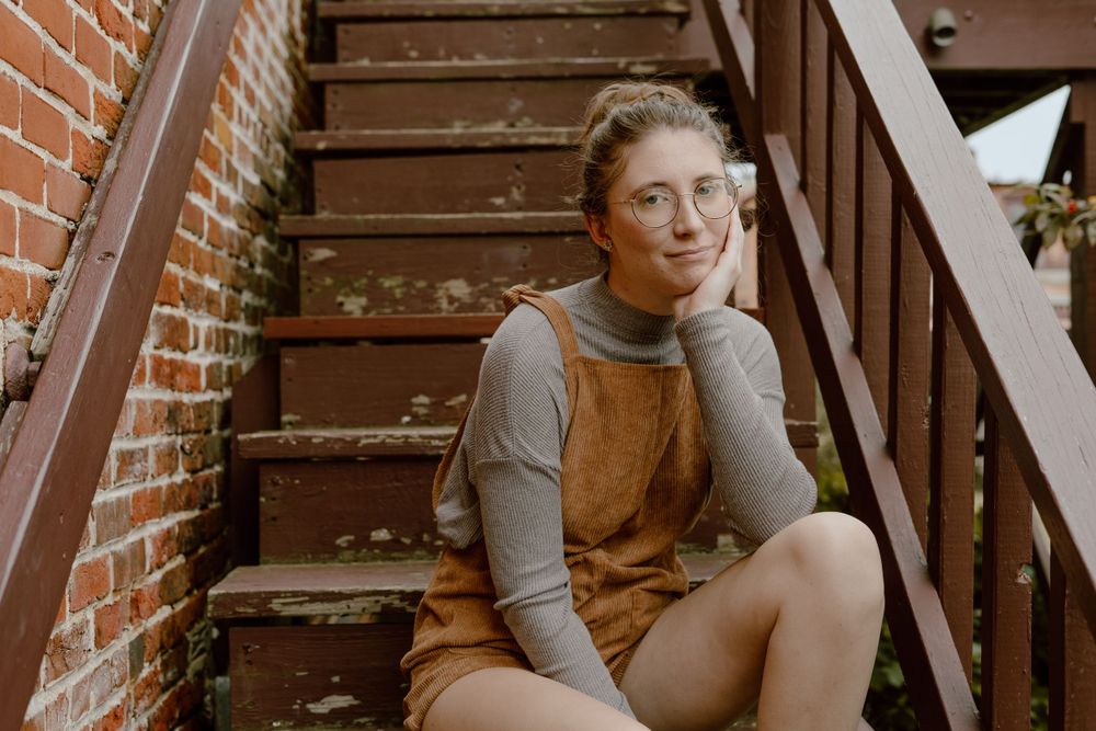 Person rests on wooden stairs against brick wall wearing grey sweater.