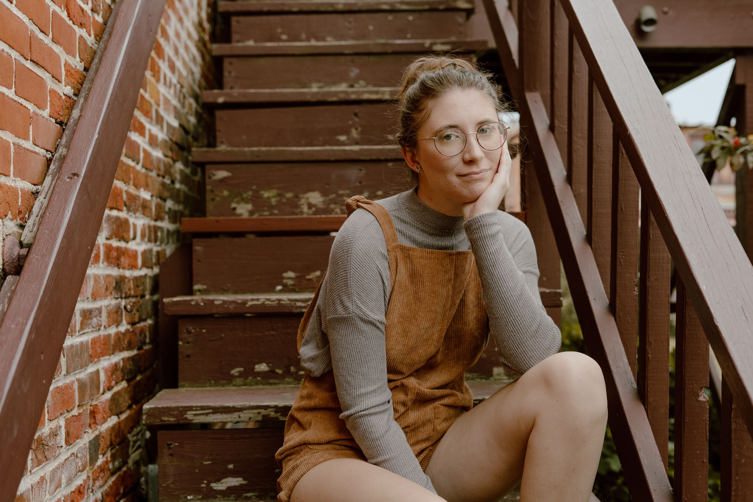 Person rests on wooden stairs against brick wall wearing grey sweater.