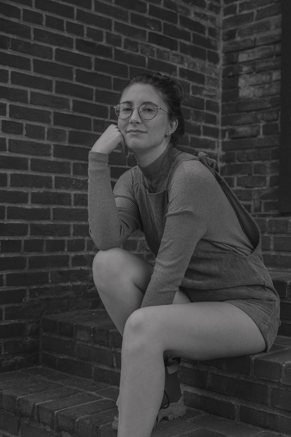 Figure in casual attire sits contemplatively on brick steps in black and white.