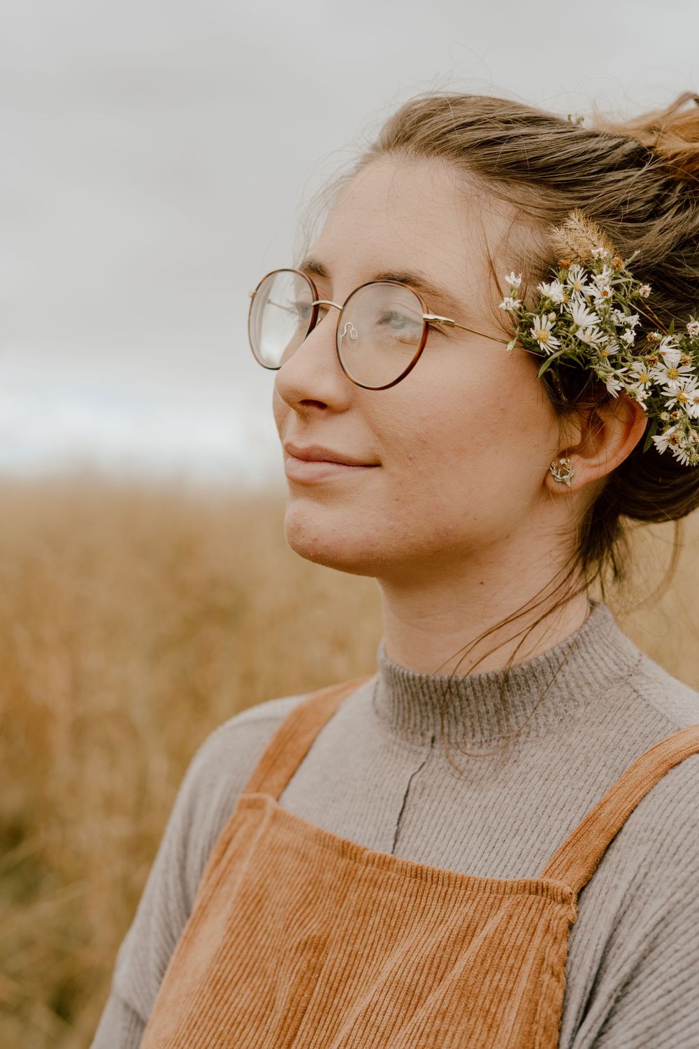 Side profile portrait with glasses and baby's breath flowers in hair against natural backdrop.