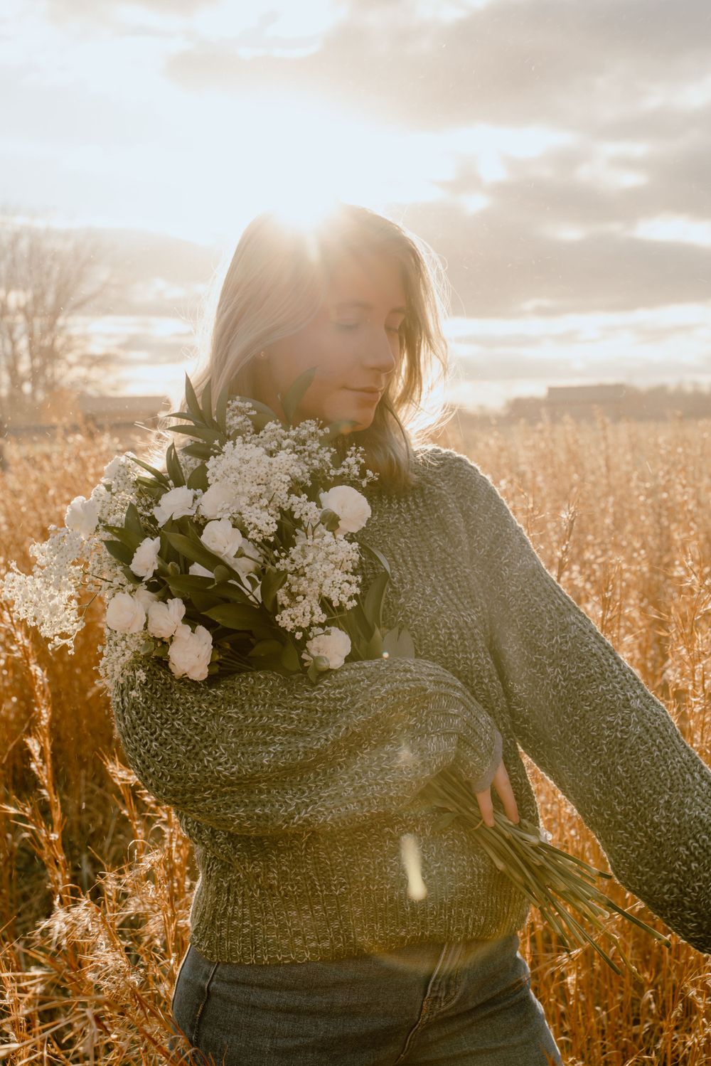 Person in sweater with floral crown dances in golden sunlit field at sunset.