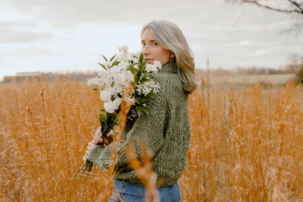 Figure in green sweater stands among autumn wildflowers in golden light.