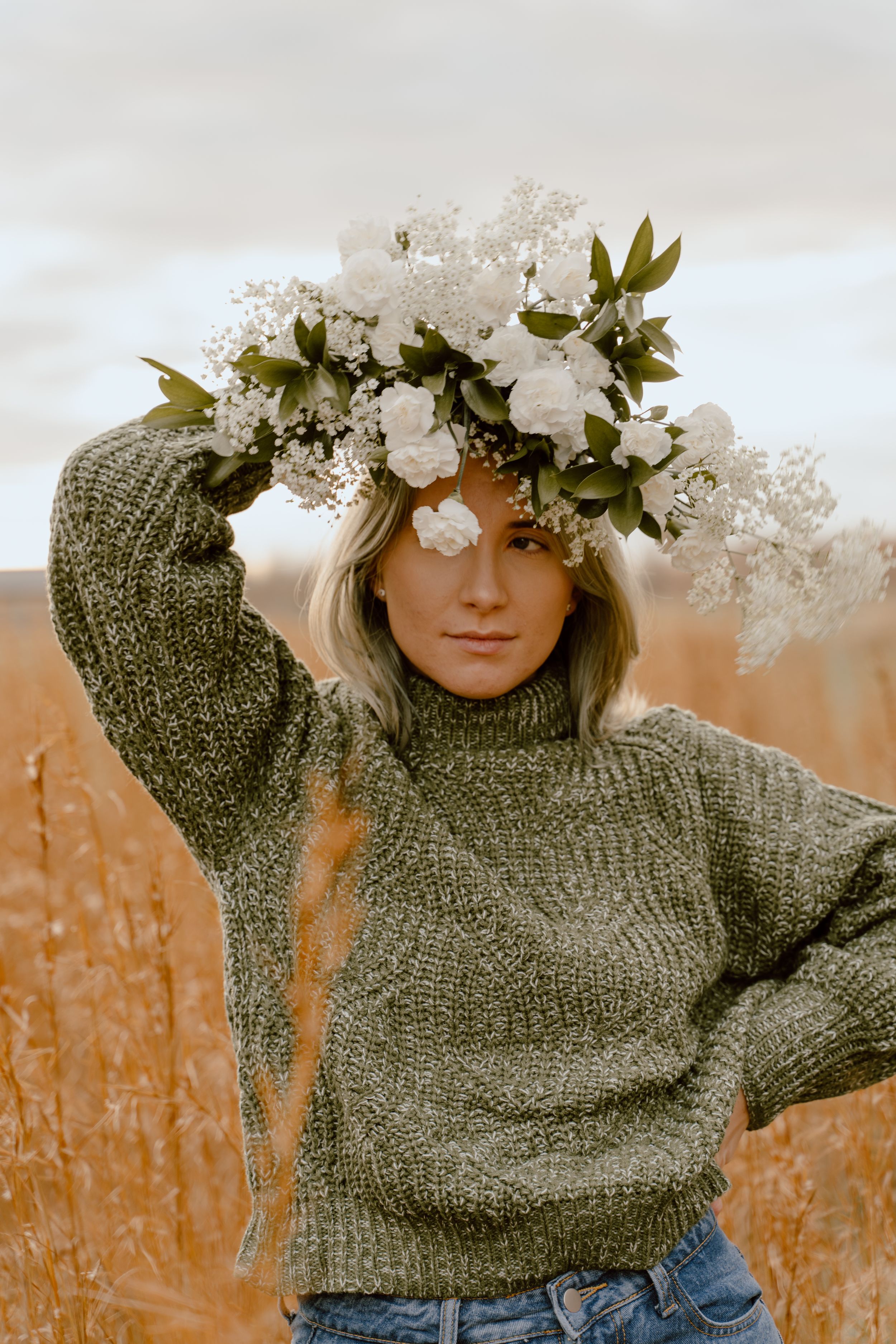 Elegant white floral crown contrasts with sage green sweater against a warm golden backdrop.