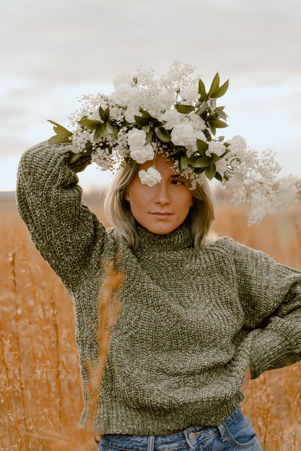 Elegant white floral crown contrasts with sage green sweater against a warm golden backdrop.