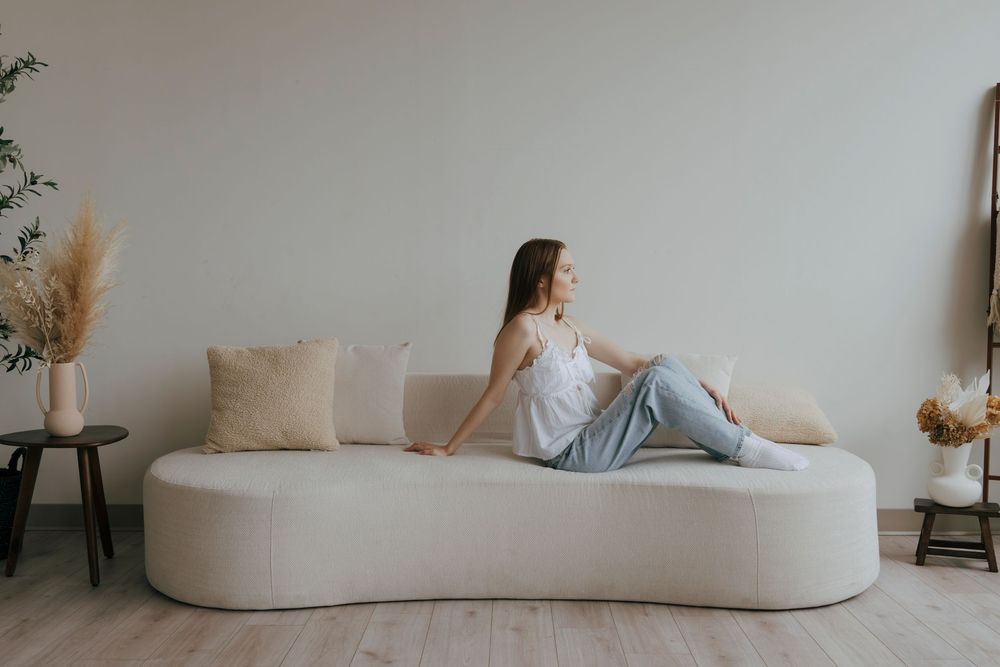Woman relaxing on a modern curved white sofa with neutral cushions in a minimalist living room.