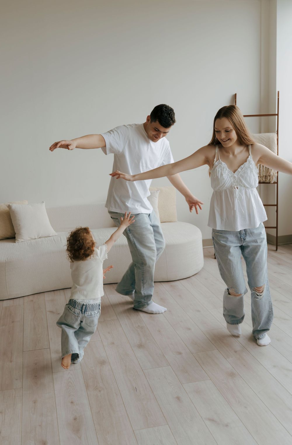 A happy young family with a toddler dancing and playing together in a bright modern living room.