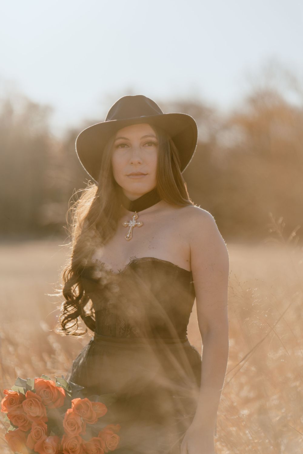 A golden hour portrait featuring a black hat and corset in a rustic field setting.