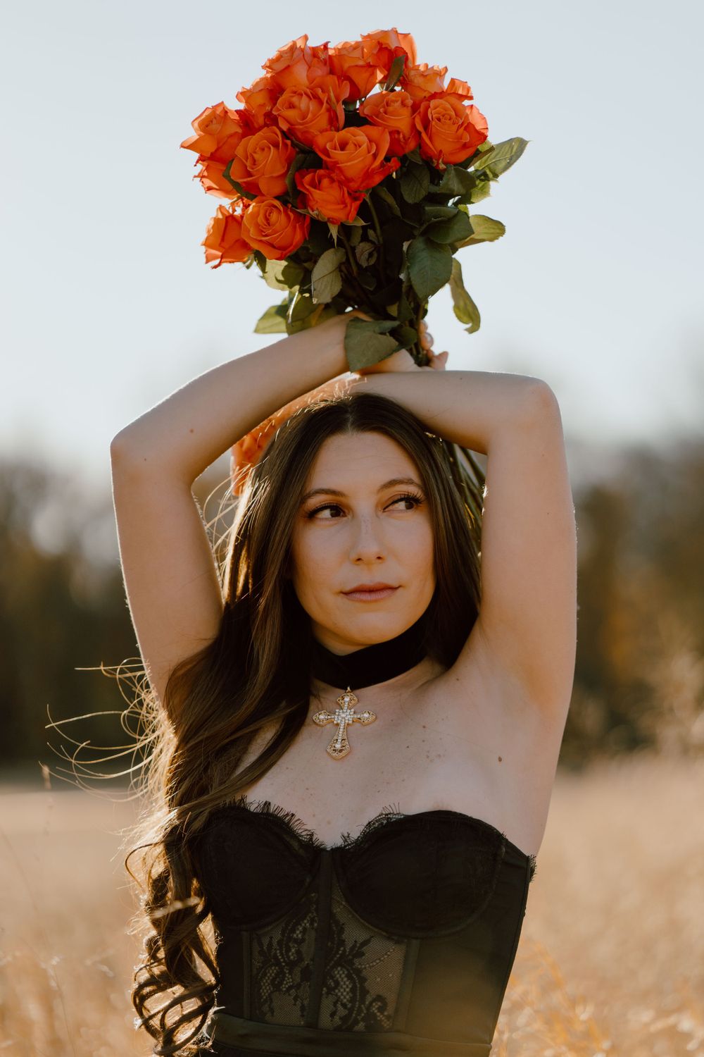 A dramatic portrait with red roses held overhead in golden sunset light.