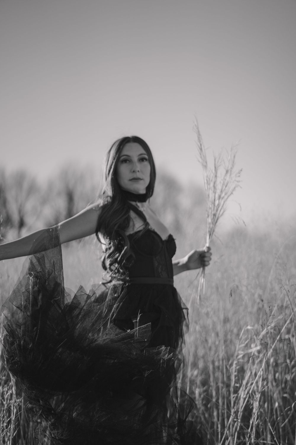 A black and white portrait showing a flowing dark dress in a field of tall grass.