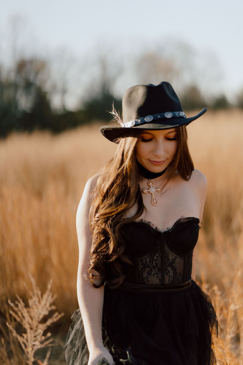 A black dress and decorative hat create a moody autumn portrait in a golden wheat field.