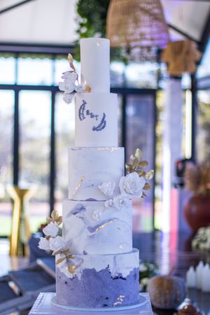 Elegant five-tier marble-effect wedding cake decorated with white flowers and blue watercolor details.