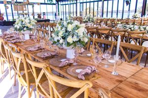 Rustic wedding reception table setting with wooden chairs and white floral centerpieces.