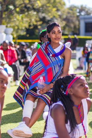 Young woman wearing vibrant red and blue patterned dress at outdoor cultural event.
