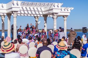 Crowd gathered under white pergola by waterfront during cultural celebration.