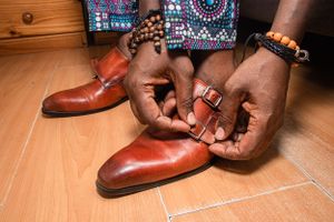 Brown leather dress shoes being fastened on wooden flooring.