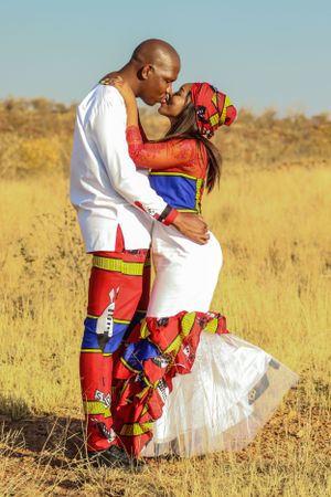 A romantic couple in traditional African wedding attire poses in a sun-lit savanna field.