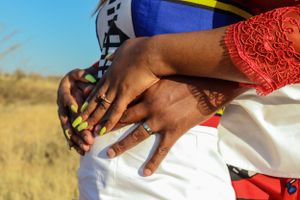 Close-up of hands with colorful manicured nails against white and red traditional clothing.