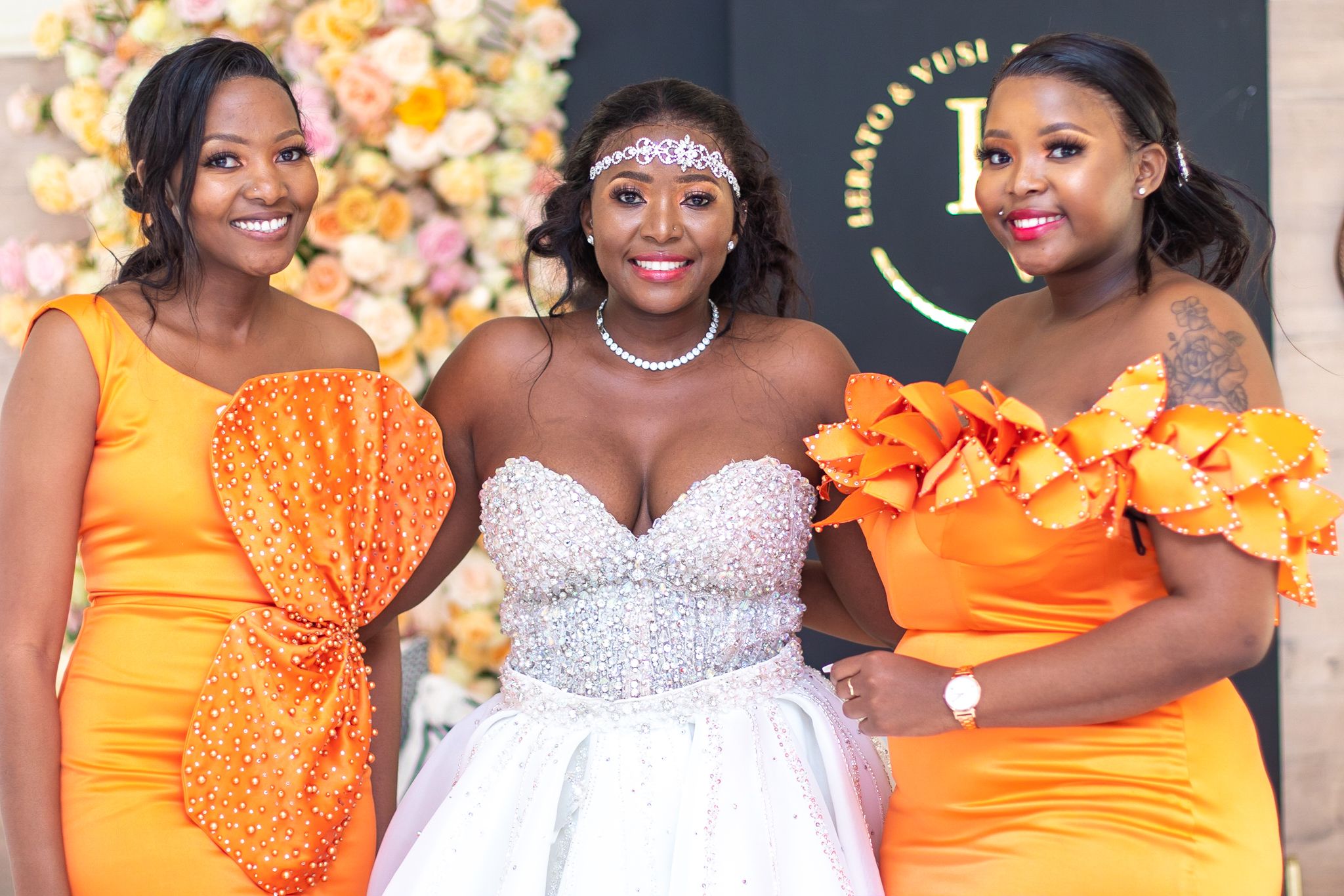 Wedding party members pose in coordinated orange dresses and a white gown.