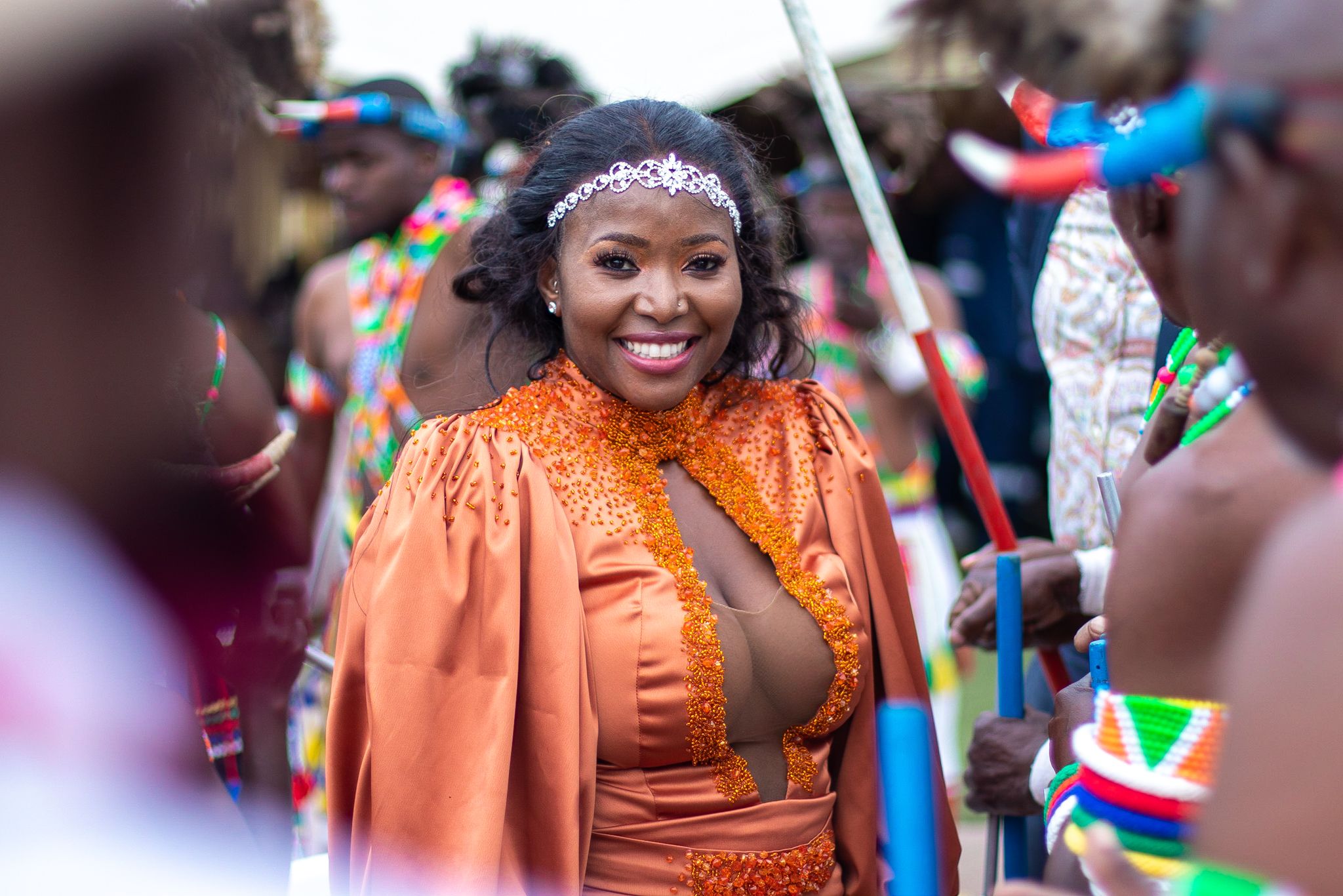 Wedding celebration guest wearing a festive orange dress with traditional accessories at an outdoor event.