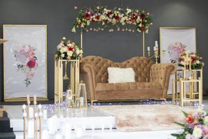 Elegant wedding reception setup with floral arch, tufted sofa, and gold decor elements.