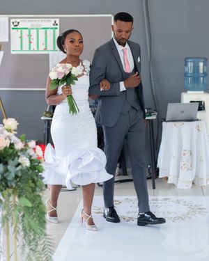Couple walking down decorated aisle in white dress and gray suit during wedding ceremony.