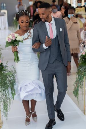 Newlyweds walking down floral-lined aisle in classic wedding attire.