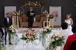 Elegant wedding ceremony setup with floral arrangements, candles, and a tan couch on a decorated stage.
