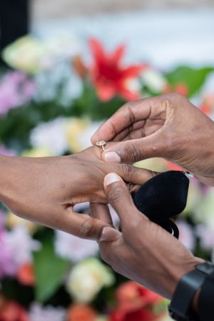 Close-up shot of hands exchanging wedding rings with colorful flowers in the background.