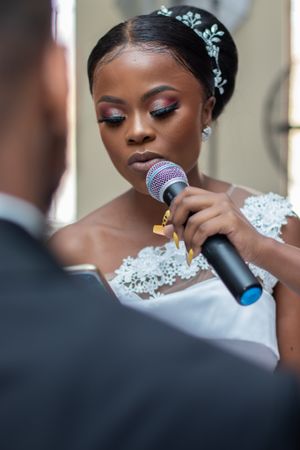 Close shot of someone holding a microphone while wearing a delicate tiara and lace dress.