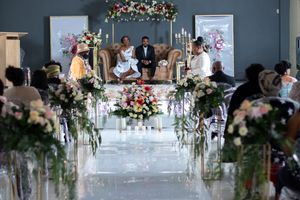 An elegant wedding ceremony setup with floral aisle decorations and white chairs in an indoor venue.