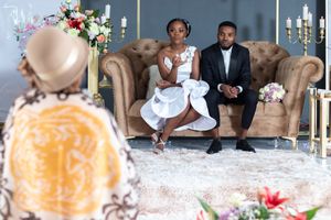 Wedding couple posing on a brown couch surrounded by floral arrangements and candelabras.
