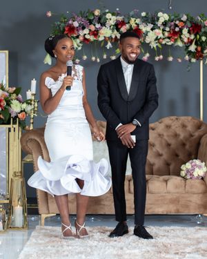 A couple poses together during their wedding celebration with floral decorations in the background.