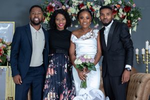 A wedding party poses together in front of a floral backdrop during the celebration.