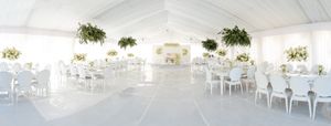 Spacious white wedding reception tent with elegant white chairs and floral decorations.